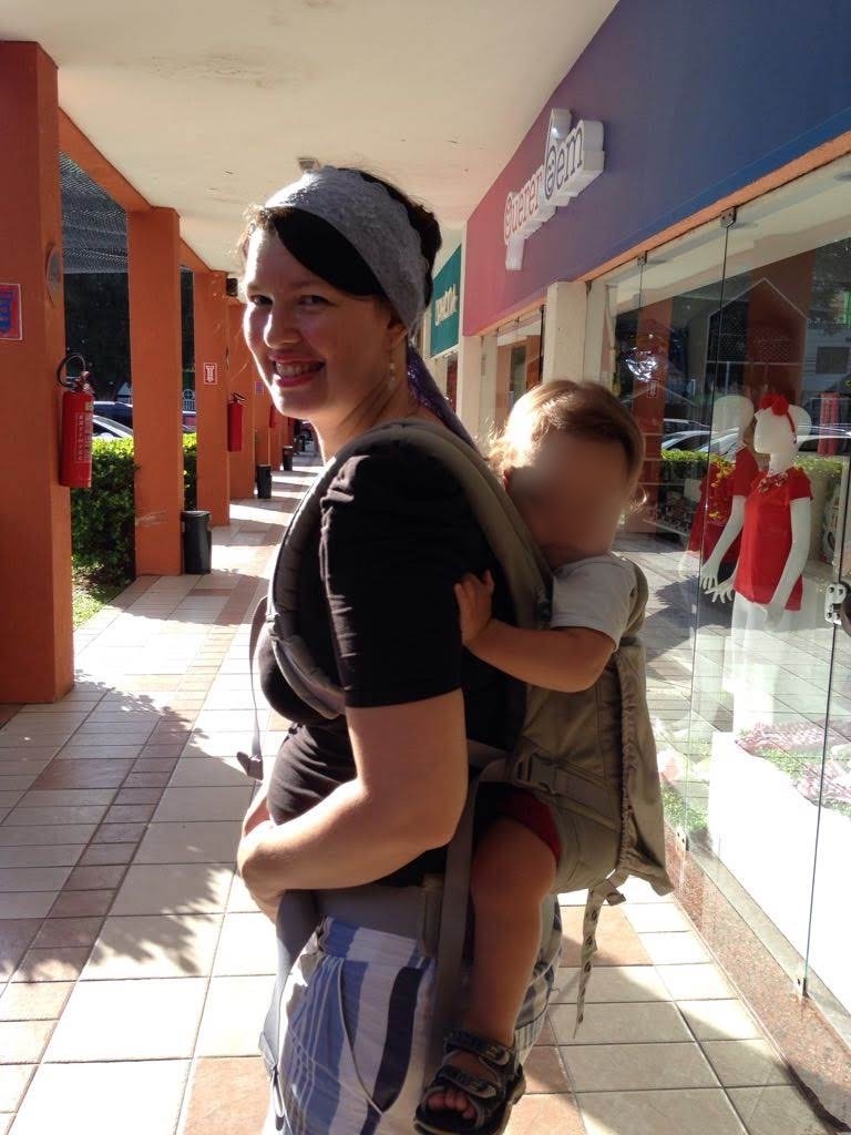 Josie Zecchinelli em galeria de lojas carregando o filho maiorzinho nas costas em mochila ergonômica