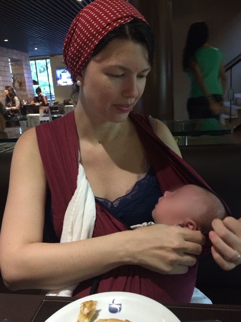 Filho da Josie Zecchinelli dormindo tranquilo no sling durante refeição em restaurante